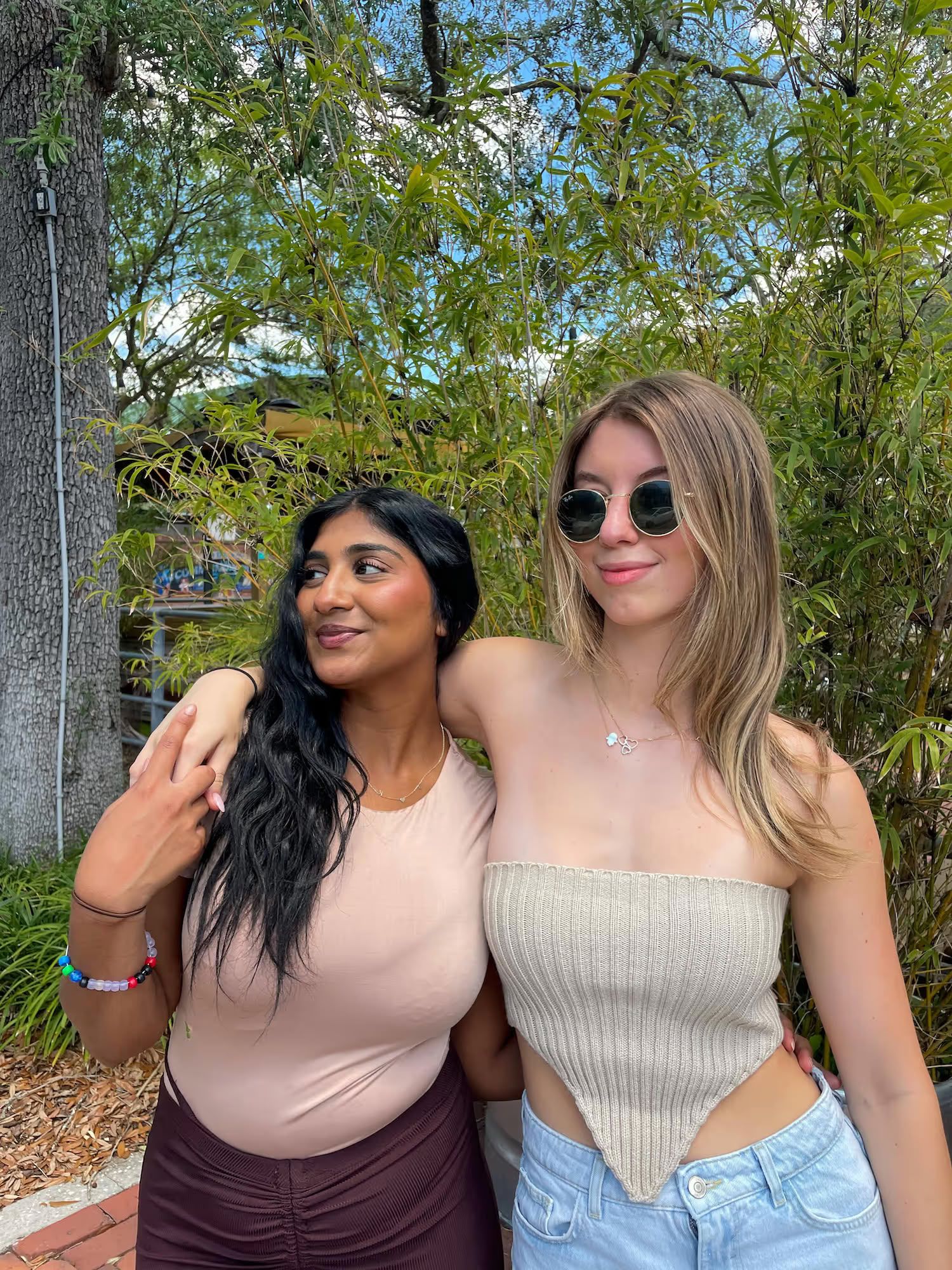 Ufora Student Living Apartments Two young women standing close together outdoors, smiling, with greenery in the background.